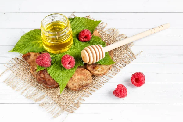 Le bol avec du miel, des baies et des feuilles de framboise sur un support en bois. Cuillère au miel — Photo