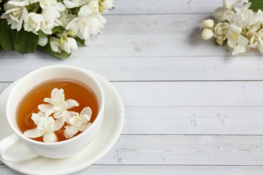 Bir bardak çay, bir ışık ahşap arka plan üzerinde bir kavanoz içinde bir kaşık, Yasemin çiçekleri bal dökme. Kopya alanı