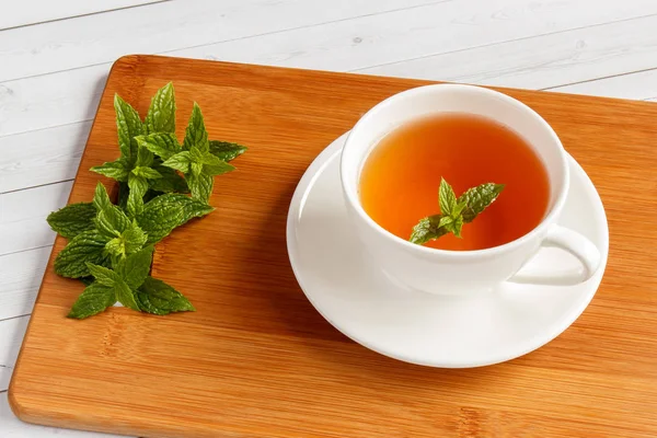 Ένα φλιτζάνι τσάι μέντας σε ένα ξύλινο τραπέζι με φύλλα φρέσκου δυόσμου, ρηχό βάθος πεδίου και επιλεκτική εστίαση — Φωτογραφία Αρχείου