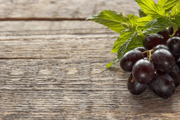 Raisins noirs mûrs avec des feuilles, sur fond de bois. Concentration sélective. Espace de copie . — Photo