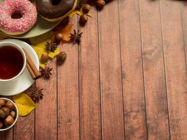 Rosquillas de colores en el plato de otoño y una taza de té, el diseño sobre fondo de madera rústica. Copiar espacio — Foto de Stock