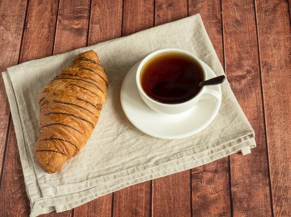 Desayuno croissant y té en una servilleta textil. Fondo de madera oscura . — Foto de Stock