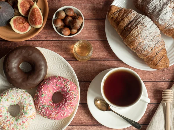 Desayuno donut croissant higos nueces en los platos y té Copa en la mesa — Foto de Stock