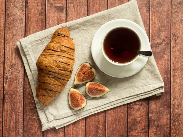 Desayuno croissant y té en una servilleta textil. Fondo de madera oscura . — Foto de Stock