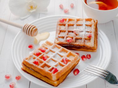 Hafif ahşap arka plan beyaz bir tabakta bal ve nar tohumları ile lezzetli ağız sulandıran Viyana waffle
