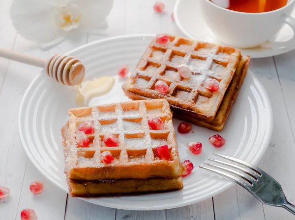 Köstliche Wiener Waffeln mit Honig und Granatapfelkernen auf weißem Teller, heller Holzgrund — Stockfoto