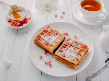 Hafif ahşap arka plan beyaz bir tabakta bal ve nar tohumları ile lezzetli ağız sulandıran Viyana waffle