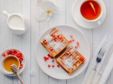 Hafif ahşap arka plan beyaz bir tabakta bal ve nar tohumları ile lezzetli ağız sulandıran Viyana waffle