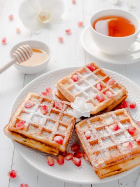 Hafif ahşap arka plan beyaz bir tabakta bal ve nar tohumları ile lezzetli ağız sulandıran Viyana waffle