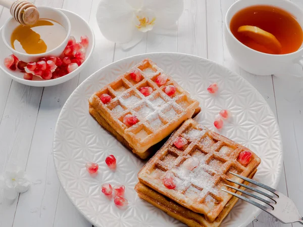 Köstliche Wiener Waffeln mit Honig und Granatapfelkernen auf weißem Teller, heller Holzgrund — Stockfoto