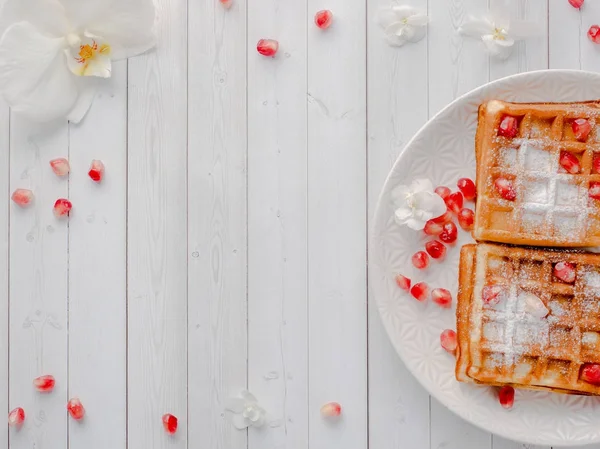 Köstliche köstliche Wiener Waffeln mit Honig und Granatapfelkernen auf einem weißen Teller, heller Holzhintergrund Kopierraum — Stockfoto
