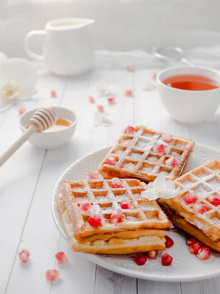 Köstliche Wiener Waffeln mit Honig und Granatapfelkernen auf weißem Teller, heller Holzgrund — Stockfoto