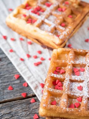 Pudra şekeri ve rustik ahşap arka plan üzerinde kırmızı kalpler ile yumuşak Viyana Belçika waffle