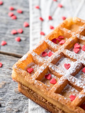 Pudra şekeri ve rustik ahşap arka plan üzerinde kırmızı kalpler ile yumuşak Viyana Belçika waffle