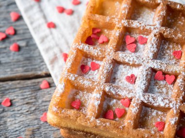Pudra şekeri ve rustik ahşap arka plan üzerinde kırmızı kalpler ile yumuşak Viyana Belçika waffle
