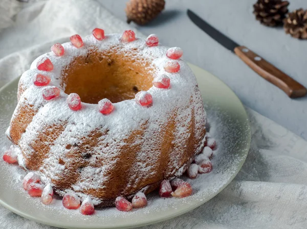 Рождественский торт в форме венка с сахарной пудрой и семенами граната на белой тарелке — стоковое фото