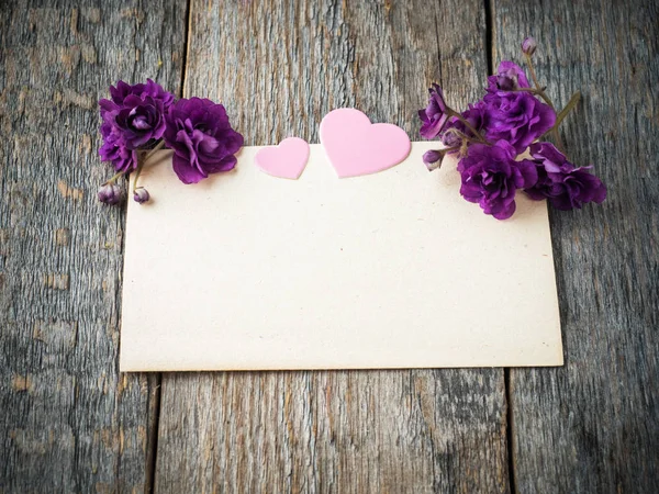 Coração de papel e flores de violetas em uma velha folha de papel no fundo de madeira rústico — Fotografia de Stock