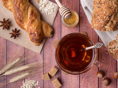 Tahıl ekmeğine bal ve fındık, bir fincan çay kahverengi şeker koyu ahşap arka plan üzerinde