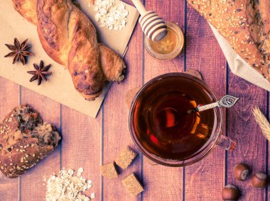 Tahıl ekmeğine bal ve fındık, bir fincan çay kahverengi şeker koyu ahşap arka plan üzerinde