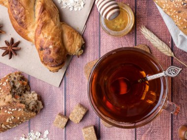 Tahıl ekmeğine bal ve fındık, bir fincan çay kahverengi şeker koyu ahşap arka plan üzerinde