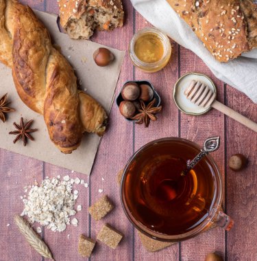 Tahıl ekmeğine bal ve fındık, bir fincan çay kahverengi şeker koyu ahşap arka plan üzerinde