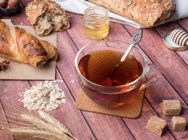 Tahıl ekmeğine bal ve fındık, bir fincan çay kahverengi şeker koyu ahşap arka plan üzerinde