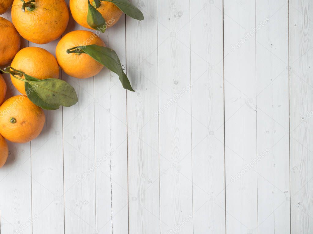Fresh mandarin or tangerines with stems and leaves on white wooden background Copy space