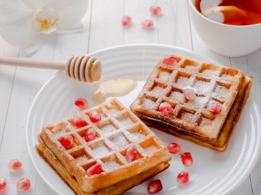 Hafif ahşap arka plan beyaz bir tabakta bal ve nar tohumları ile lezzetli ağız sulandıran Viyana waffle