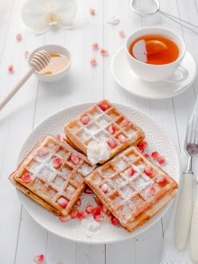 Hafif ahşap arka plan beyaz bir tabakta bal ve nar tohumları ile lezzetli ağız sulandıran Viyana waffle
