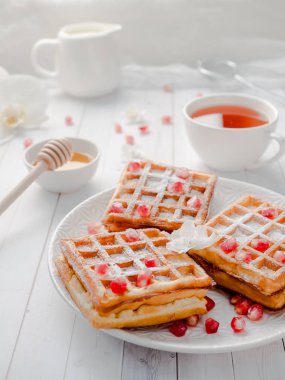 Hafif ahşap arka plan beyaz bir tabakta bal ve nar tohumları ile lezzetli ağız sulandıran Viyana waffle