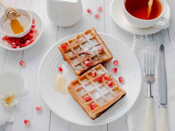 Köstliche Wiener Waffeln mit Honig und Granatapfelkernen auf weißem Teller, heller Holzgrund — Stockfoto