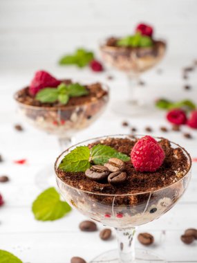 Cam kadehi naneli kahve çekirdekleri ve Beyaz ahşap masa üzerinde taze ahududu tatlı Tiramisu