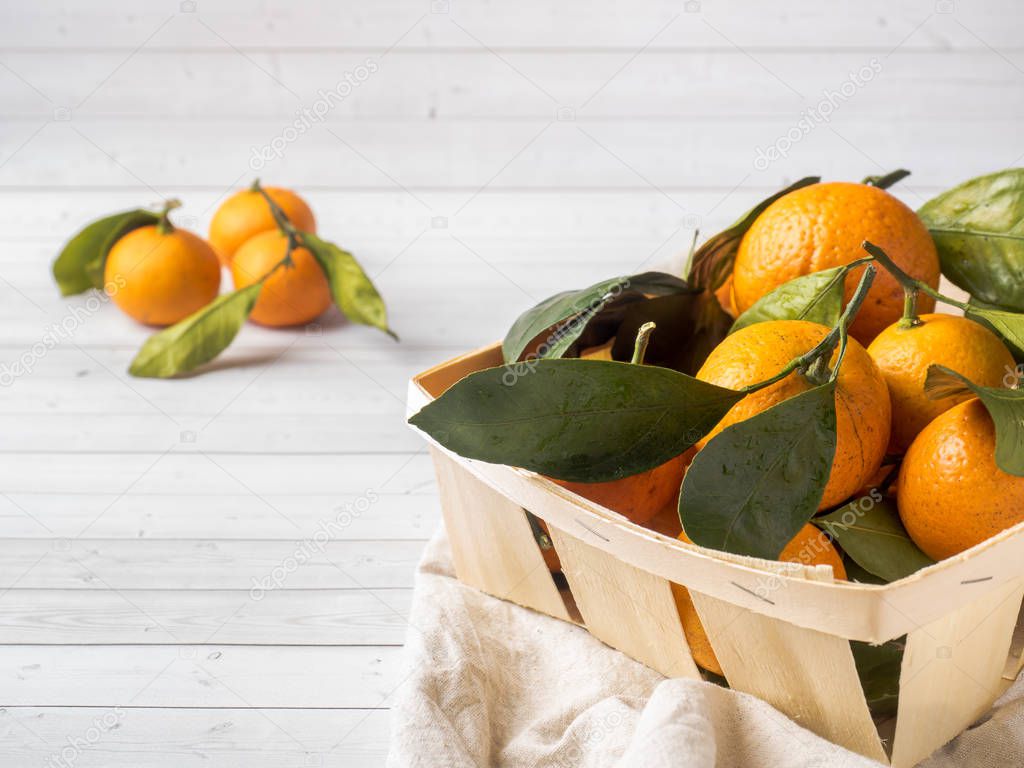 Fresh mandarin or tangerines with stems and leaves on the box on white wooden background
