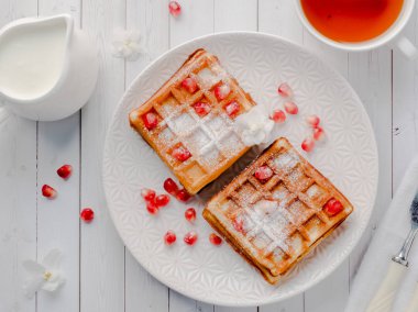 Hafif ahşap arka plan beyaz bir tabakta bal ve nar tohumları ile lezzetli ağız sulandıran Viyana waffle