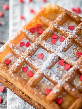 Pudra şekeri ve rustik ahşap arka plan üzerinde kırmızı kalpler ile yumuşak Viyana Belçika waffle