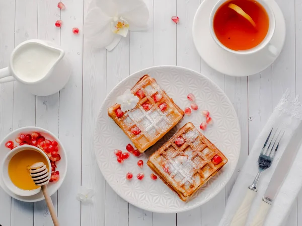 Köstliche Wiener Waffeln mit Honig und Granatapfelkernen auf weißem Teller, heller Holzgrund — Stockfoto