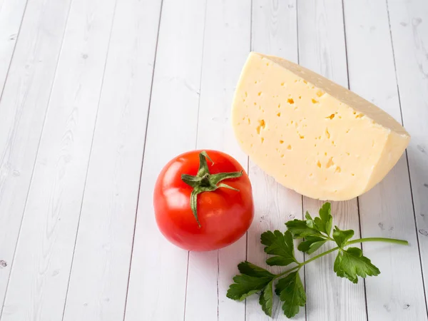 Piece of cheese with parsley and tomato on white wooden background Copy space — Stock Photo, Image