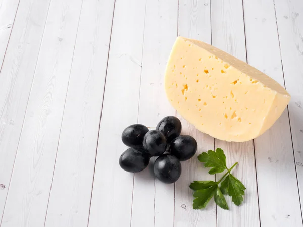 Piece of cheese with parsley and red grapes on white wooden background Copy space — Stock Photo, Image