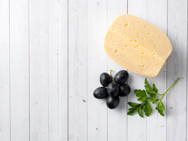 Кусочек сыра с петрушкой и красным виноградом на белом деревянном фоне — стоковое фото