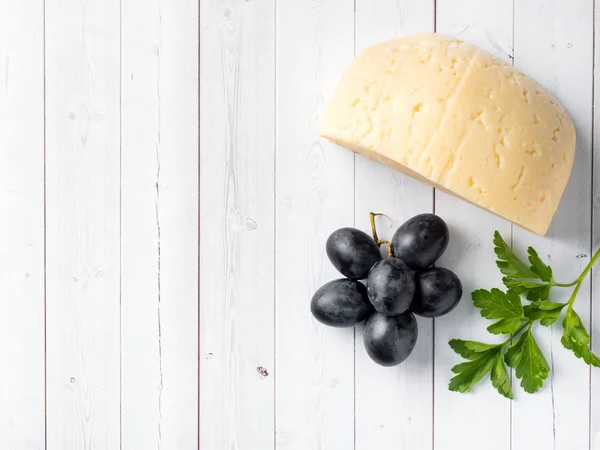 Piece of cheese with parsley and red grapes on white wooden background Copy space — Stock Photo, Image