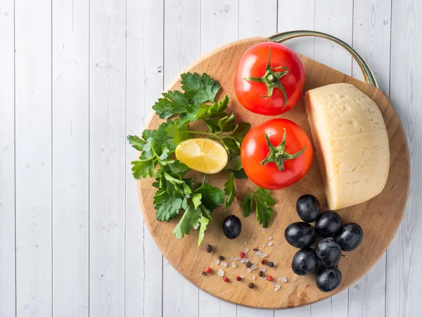 Piece of cheese with parsley, tomatoes grapes on a cutting Board. — Stock Photo, Image
