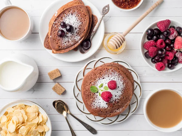 Desayuno panqueques de chocolate con bayas, una taza de café con crema, miel y cereales. Vista superior — Foto de Stock