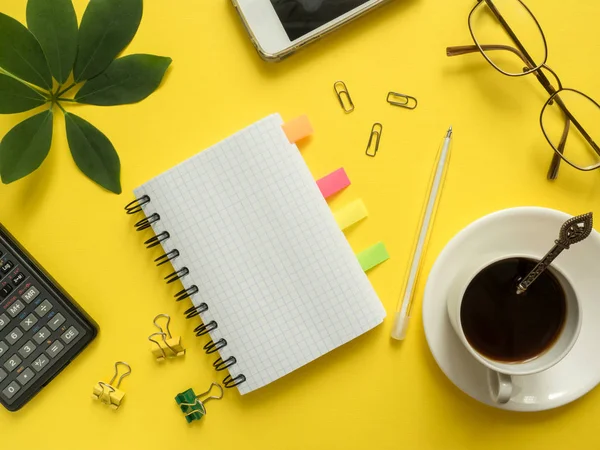 Negócios flat lay com calculadora espaço cópia, lápis, Bloco de notas, copos de café sobre fundo amarelo colorido Plantas folhas verdes — Fotografia de Stock