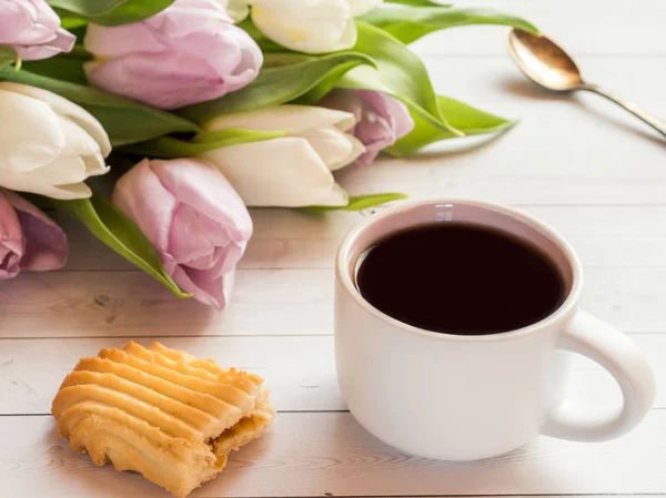 Xícara de café com biscoitos e tulipas em uma mesa de madeira — Fotografia de Stock