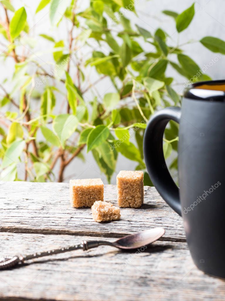 A big black mug of tea on a wooden table. Flowering plant.
