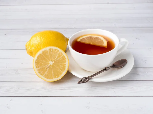Травяной черный чай в белой чашке, мед в банке свежего лимона на белом деревянном фоне — стоковое фото