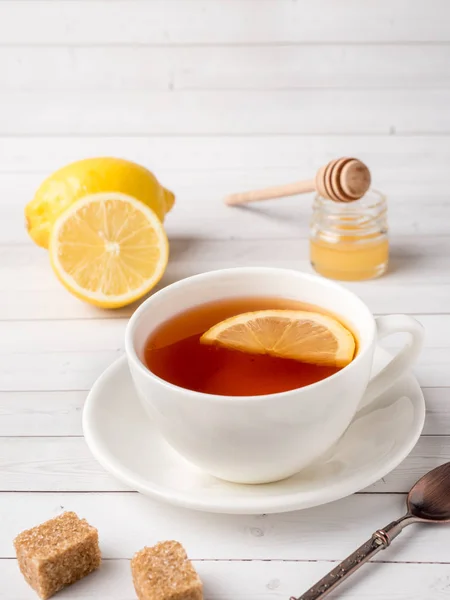 Μαύρο τσάι σε ένα λευκό φλιτζάνι, μέλι σε ένα βάζο φρέσκο λεμόνι σε άσπρο φόντο ξύλινη — Φωτογραφία Αρχείου
