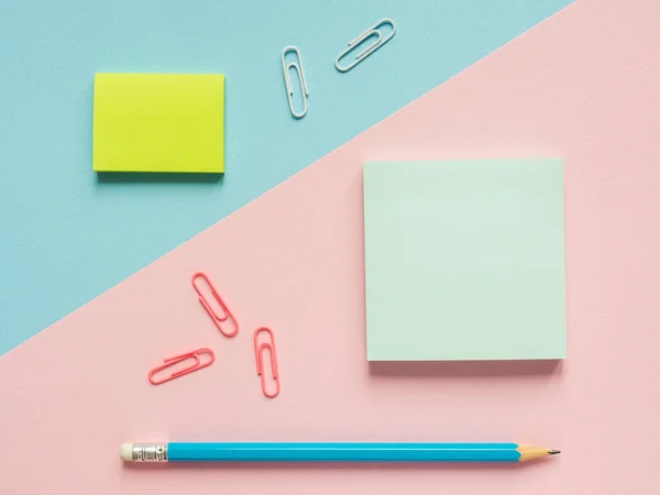 Business flat lay con espacio de copia sobre un fondo dividido en medio rosa y azul Cuadernos para escribir pegatinas de texto Lápiz, Papelería clip de papel de color . — Foto de Stock