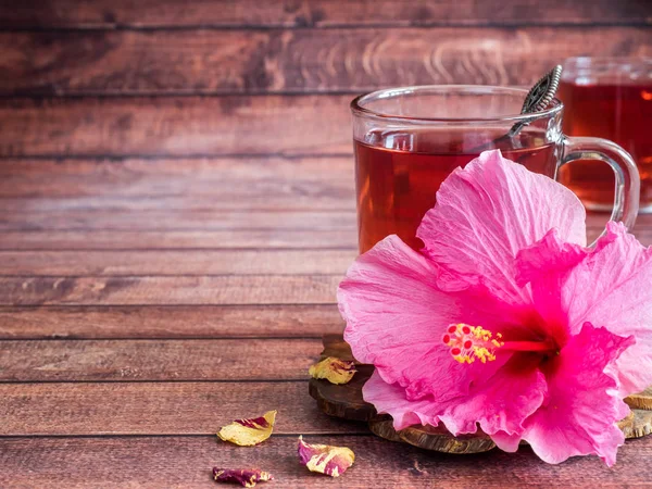 Coupe en verre avec thé rouge fleur d'hibiscus rose sur fond de bois foncé — Photo