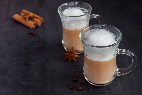 Coffee with rich milk foam in a glass beaker on a dark background sticks of cinnamon and stars of anise. Copy space